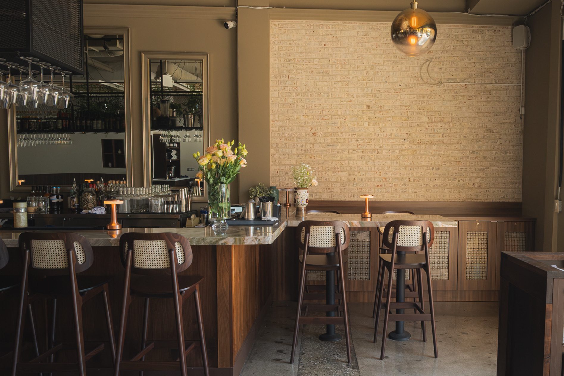 The walnut bar at Danbi, cane stools, brass pendant light and fresh flowers on the quartzite counter