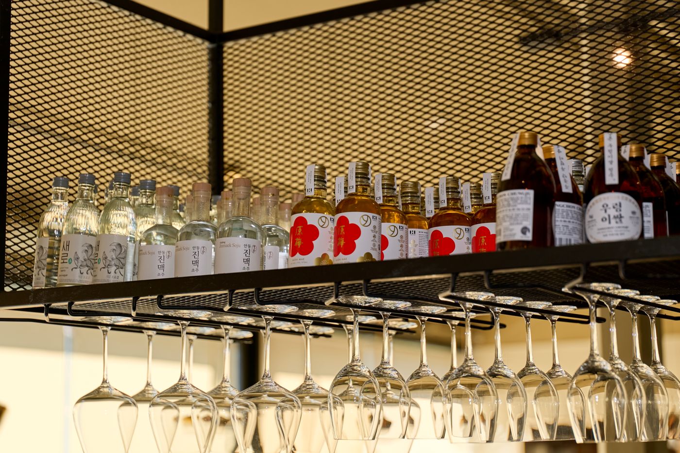 Korean soju and rice-wine bottles above the hanging glassware